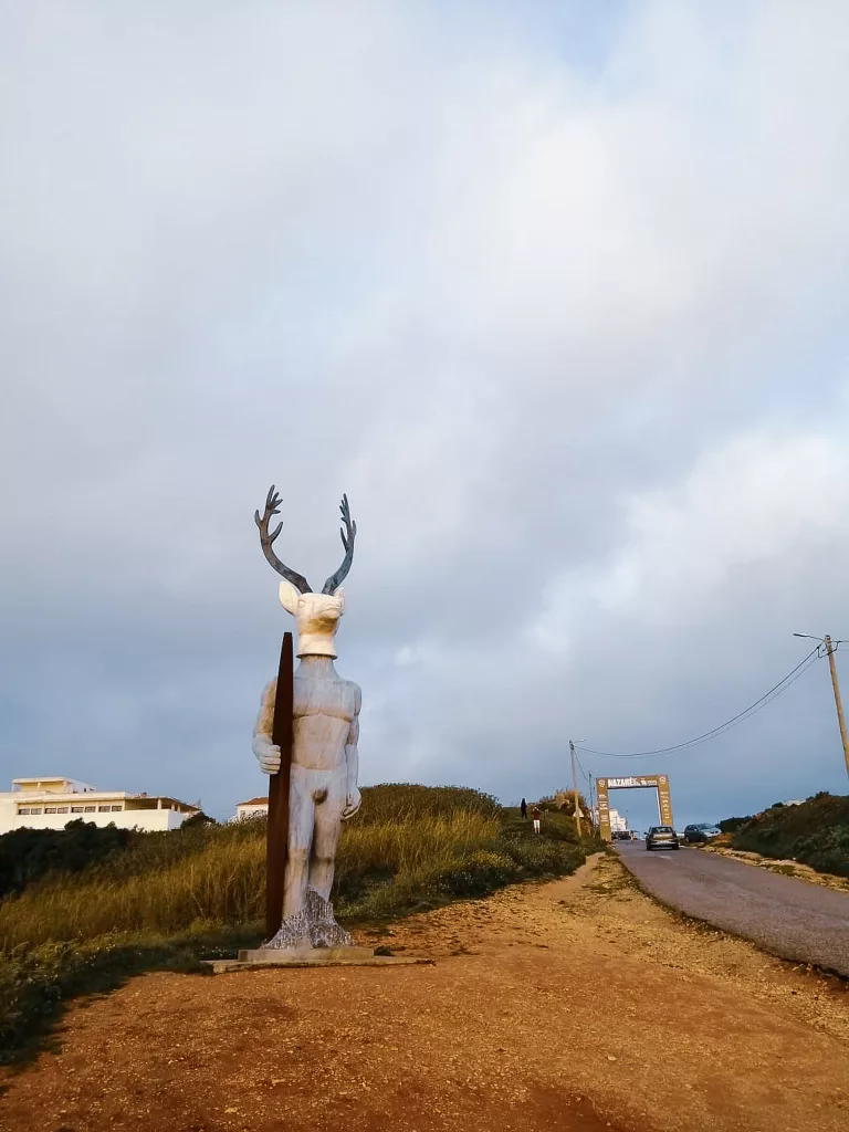 Statue eines Menschen mit dem Kopf eines Hirsches und Surfboard. Er verkörpert die Surfkultur Portugals und heißt gleichzeitig die Besucher Nazarets Willkommen.