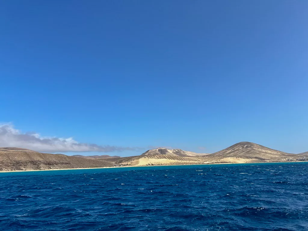 Blick vom offenen Meer auf den Sotavento Beach im Süden Fuerteventuras. Blaues Wasser vor Dünen mit einem Kitesurfer.